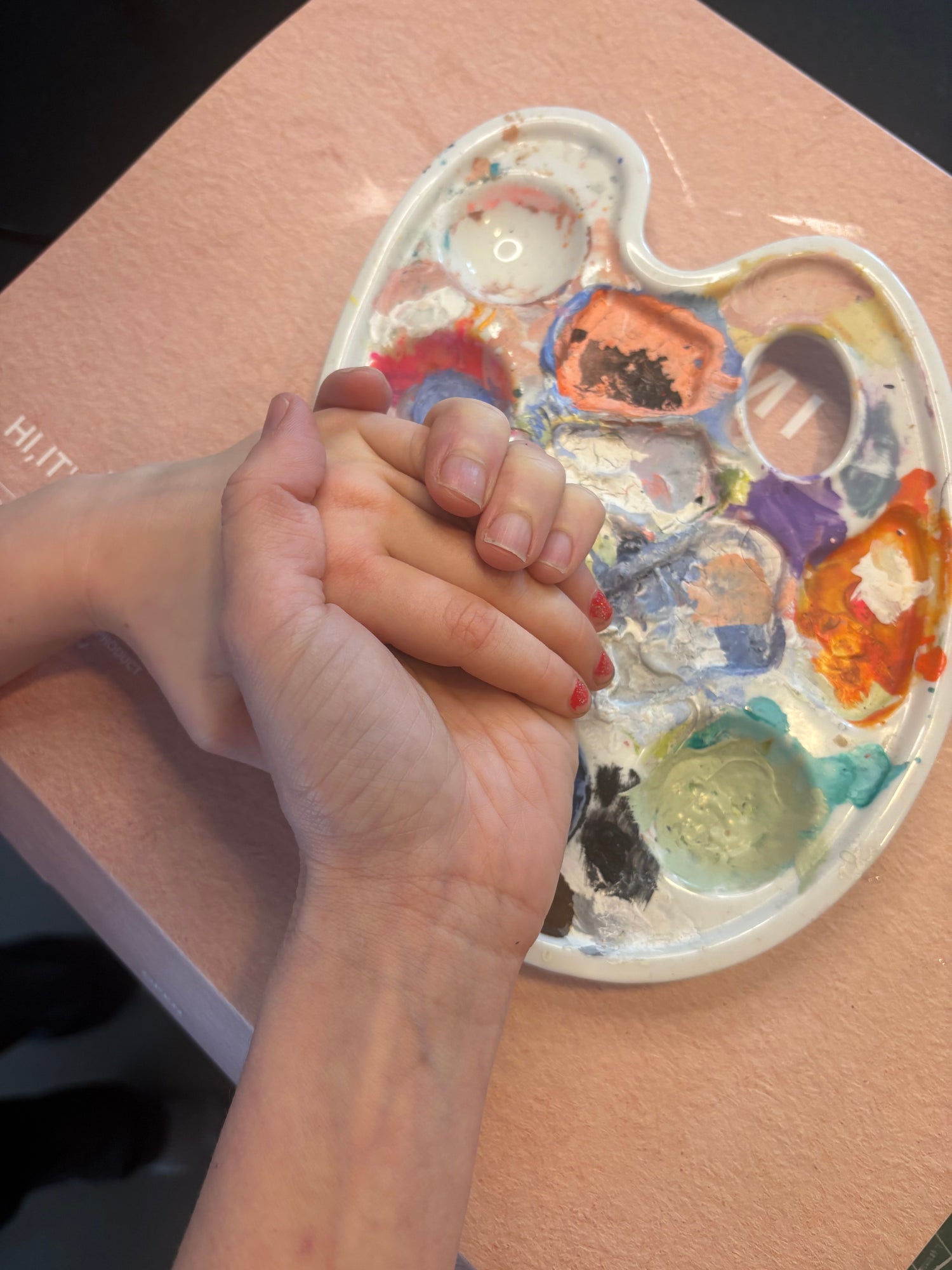 Heart-shaped paint palette with colorful paint and a hand holding a child's hand.
