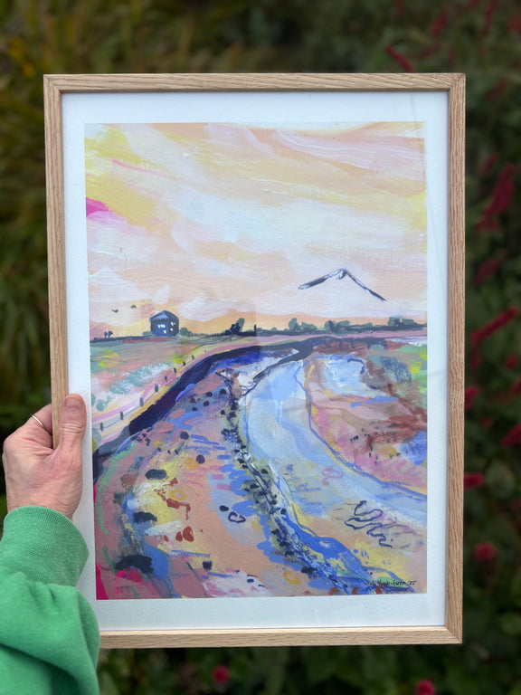 Framed colorful landscape painting held by a person outdoors.