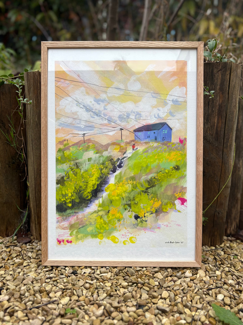 Framed painting of a colorful landscape with a blue house on a wooden stand.