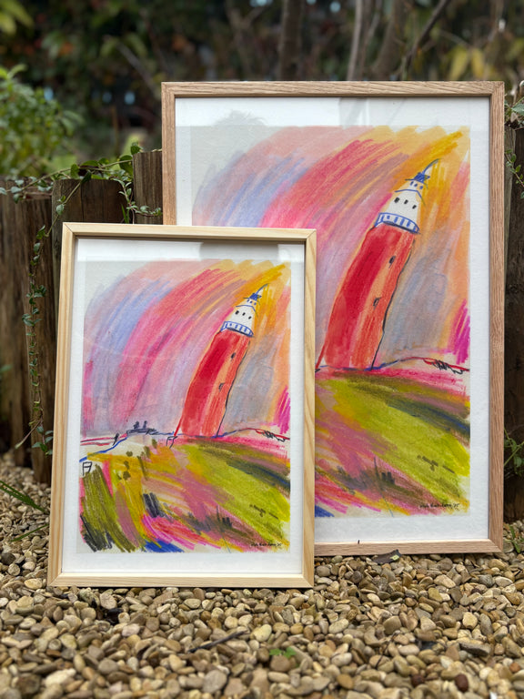 Two framed paintings of a lighthouse on pebbles with a natural background