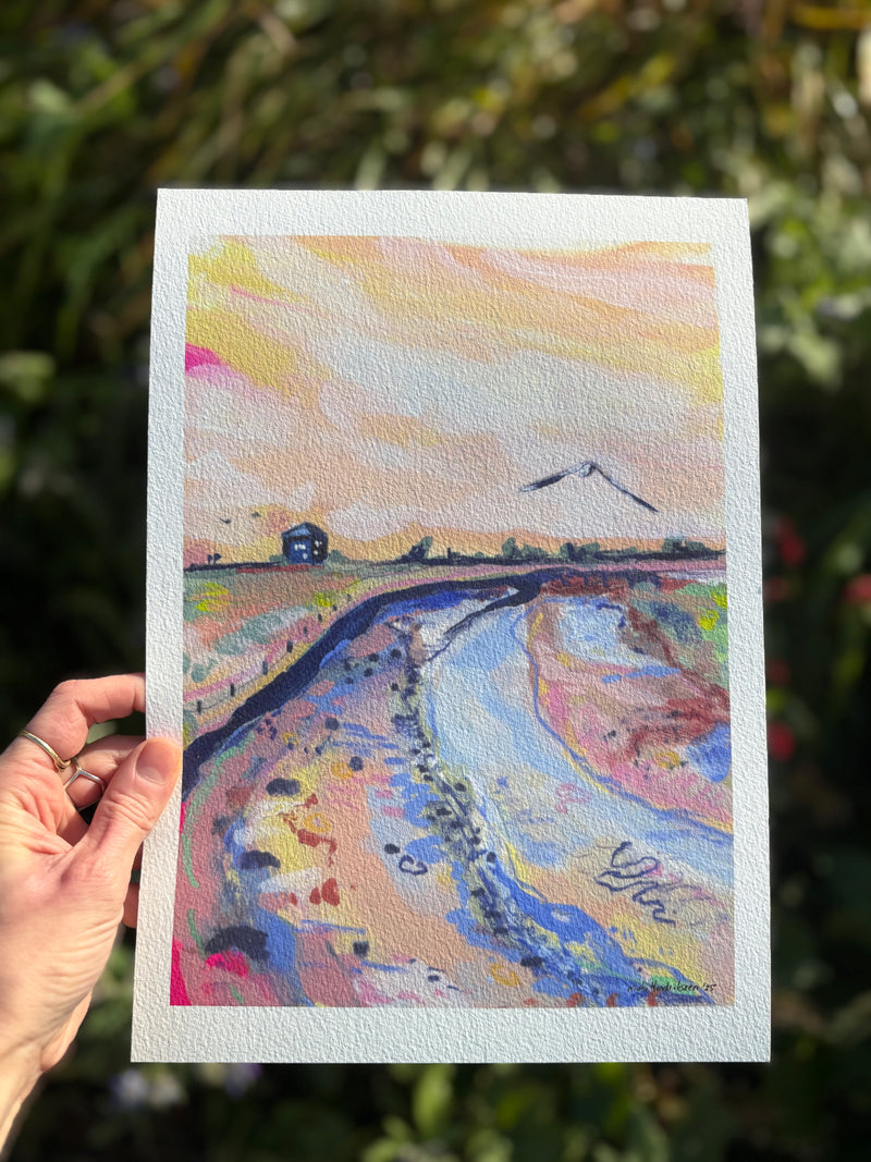 Hand holding a colorful landscape painting with a house and river.