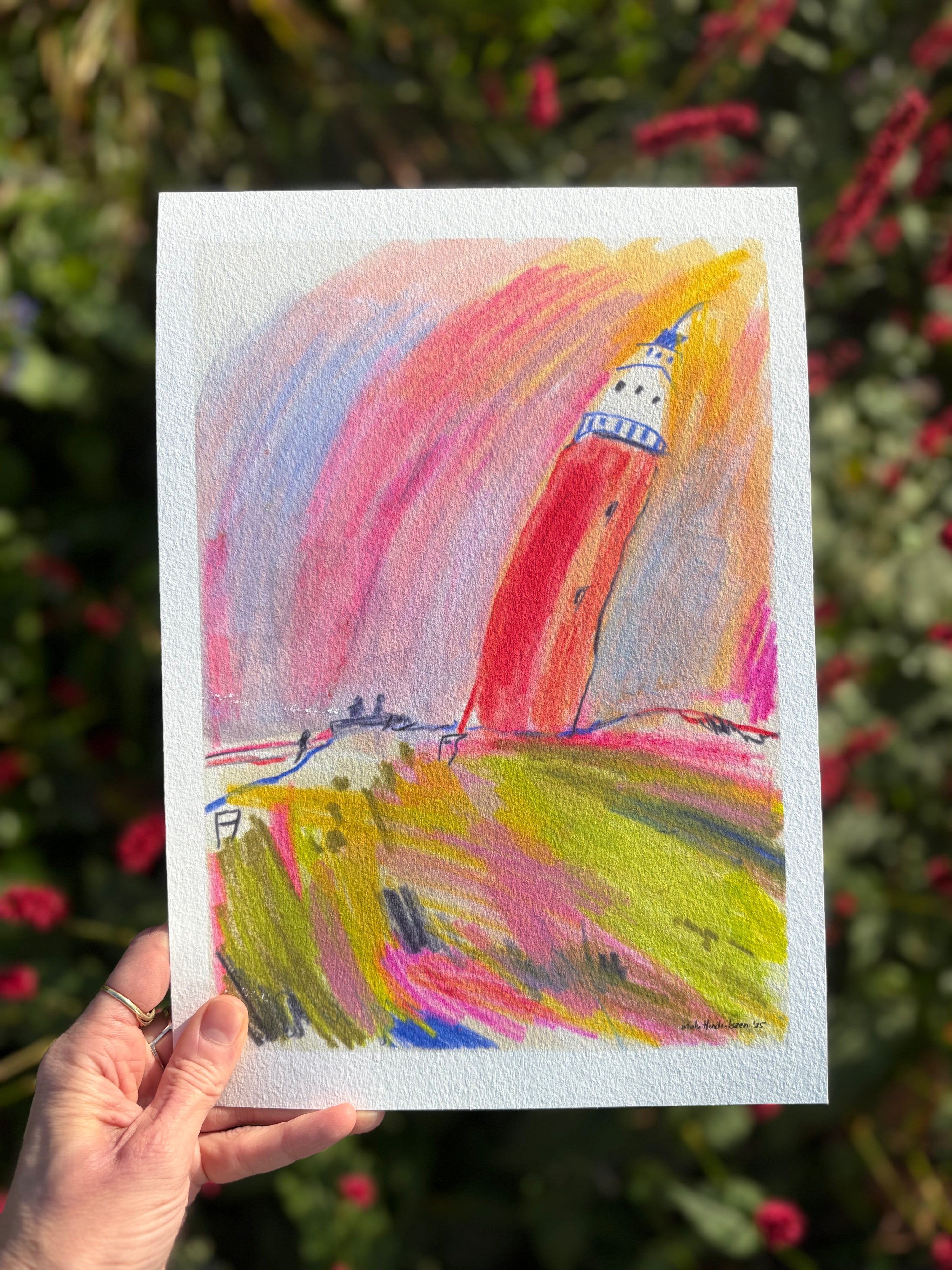 Colorful drawing of a lighthouse held by a hand with a blurred natural background
