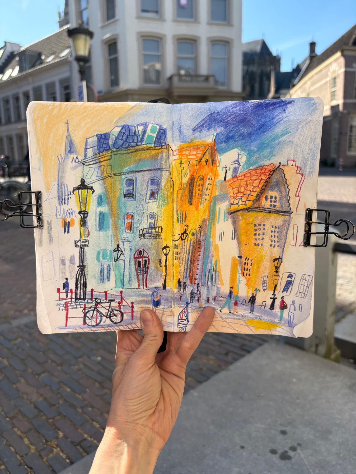 Hand holding a small painted cityscape in an urban setting