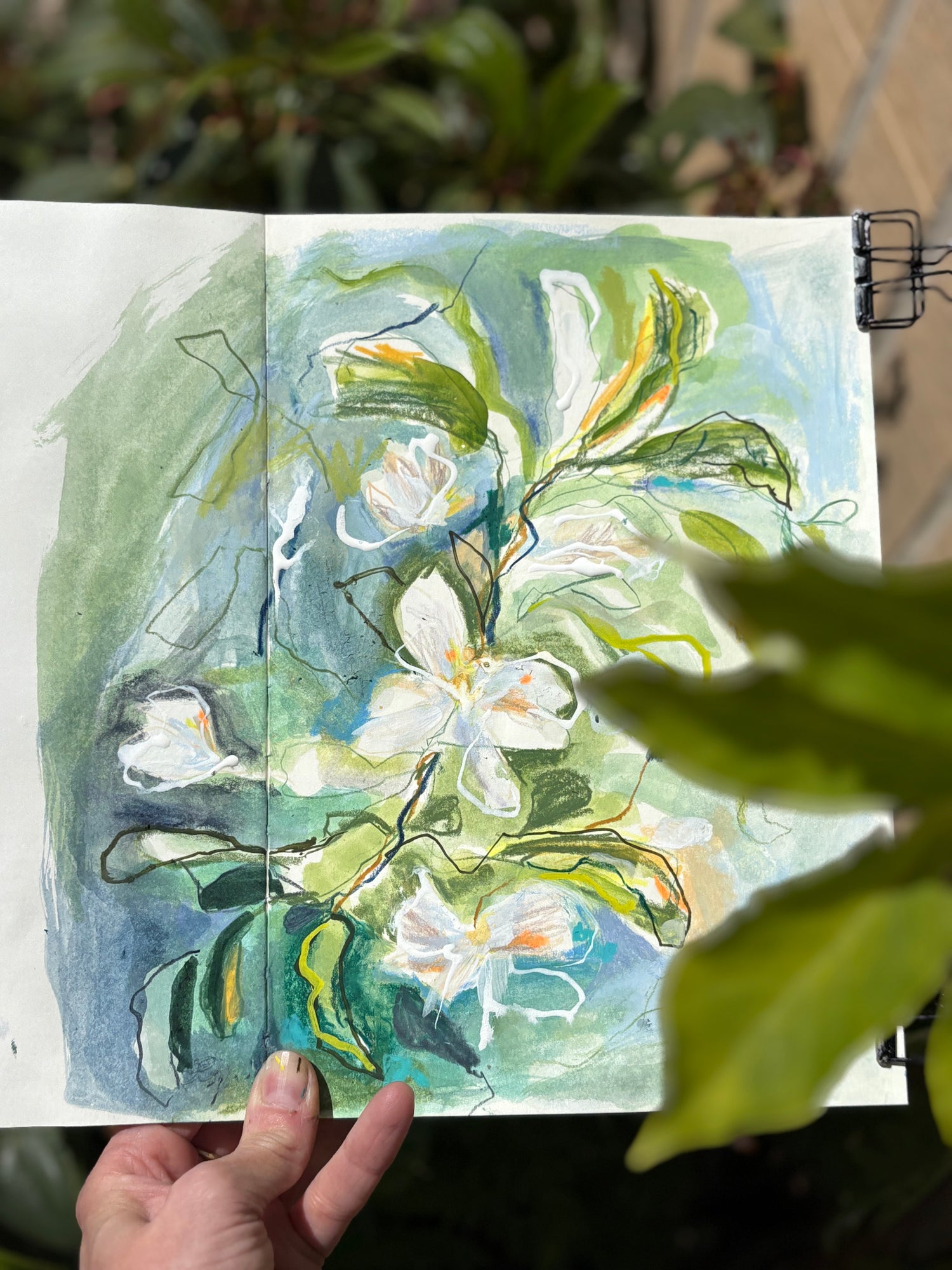 Hand holding a painting of white flowers and green leaves