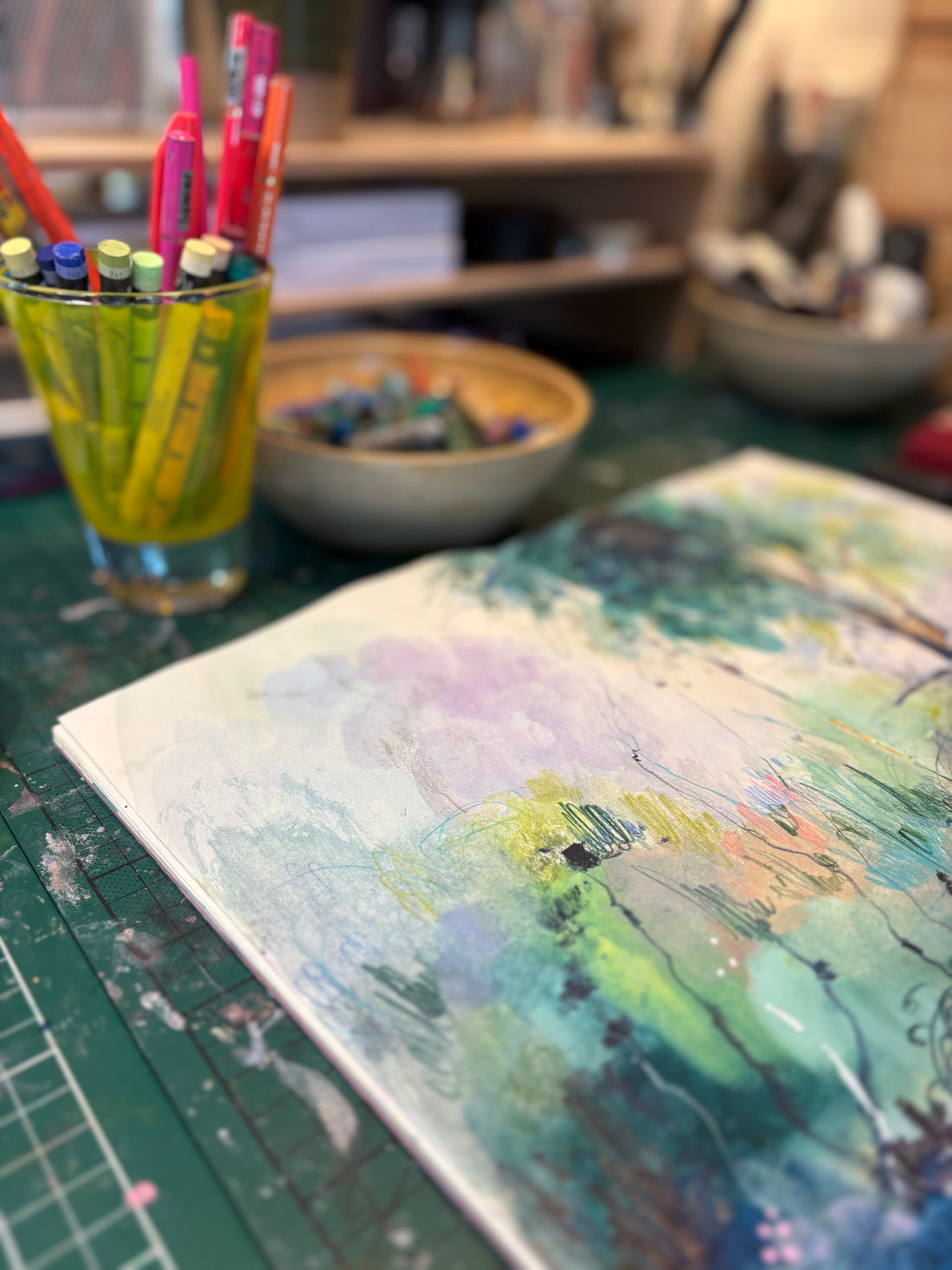 Artistic painting on paper with a glass of colored pencils and art supplies in the background.