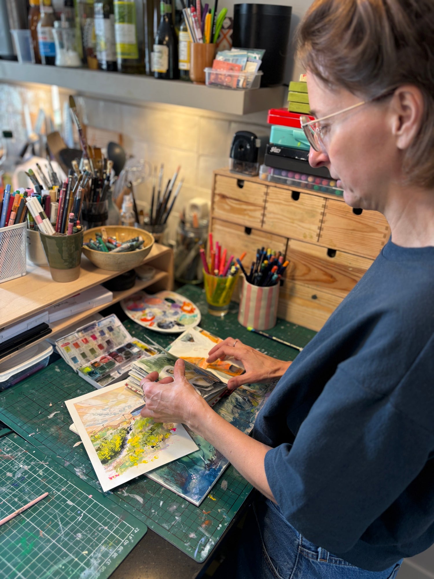 Person working on an art project at a desk with various art supplies.