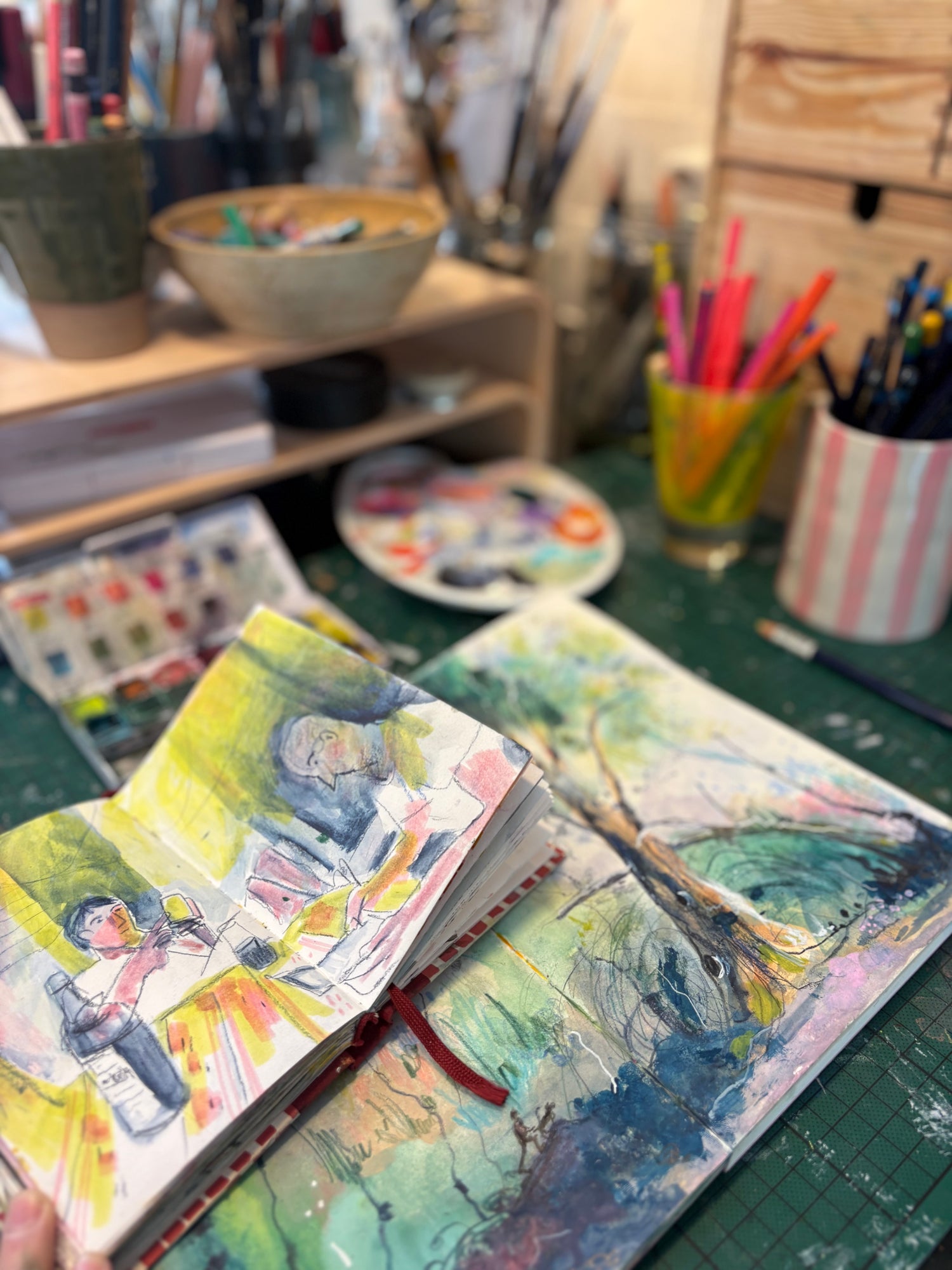 Artistic sketchbook with watercolor illustrations on a desk with art supplies.
