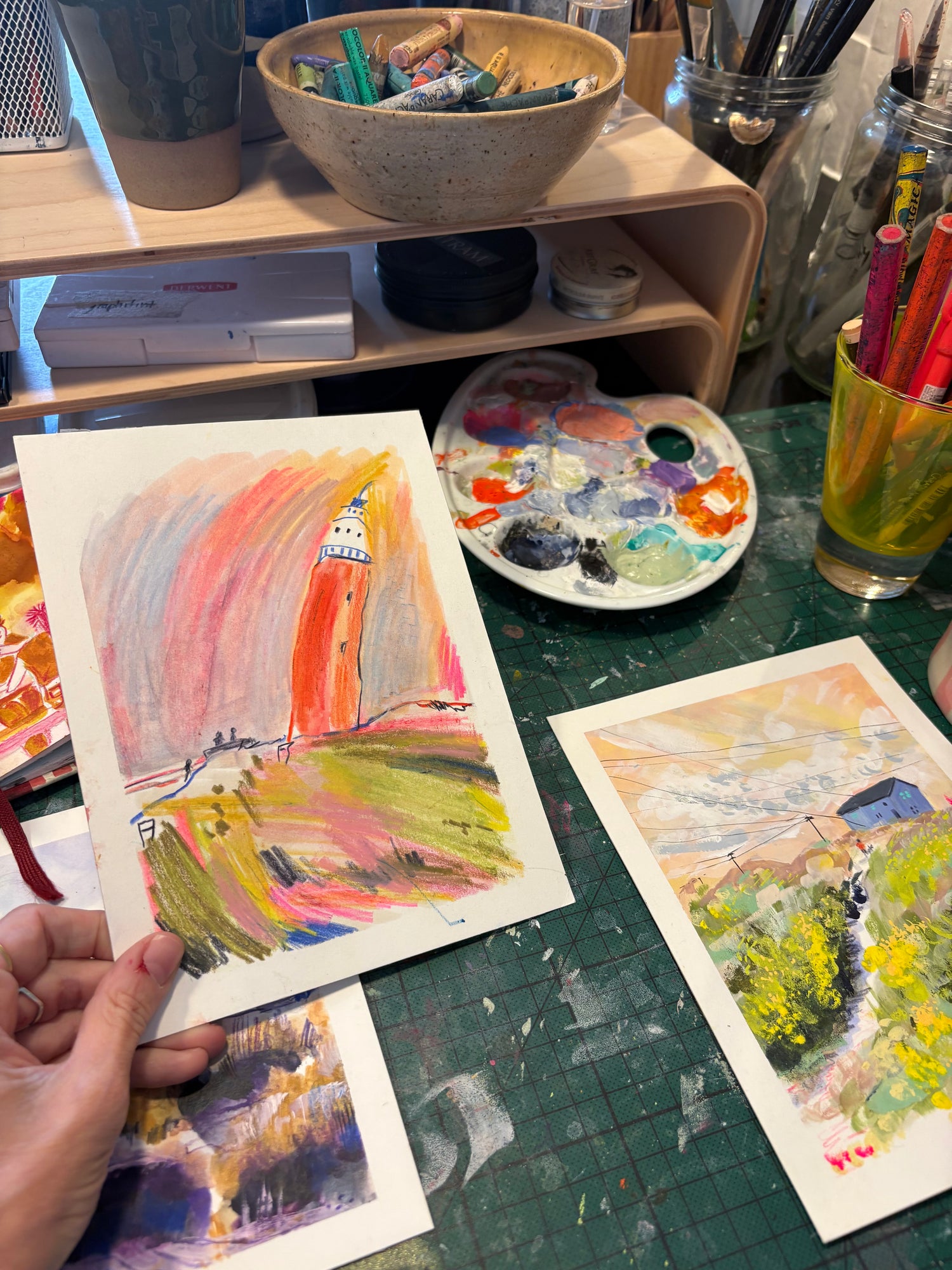 Artistic creation process with watercolor paintings and art supplies on a table.