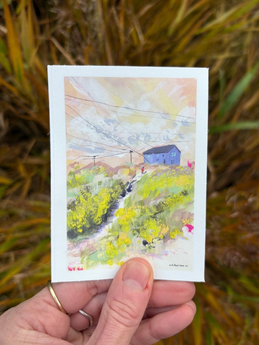 Hand holding vinyl sticker with a colorful landscape and blue house 