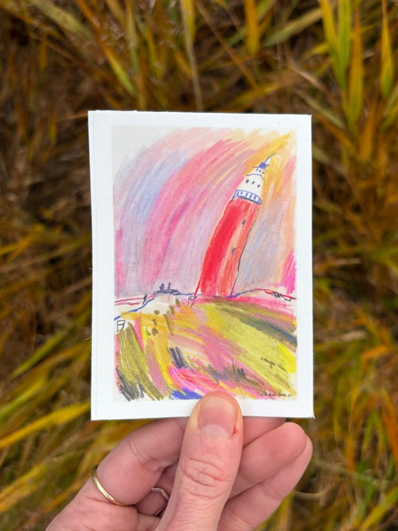 Hand holding kiss cut sticker with a colorful lighthouse painting on it. 